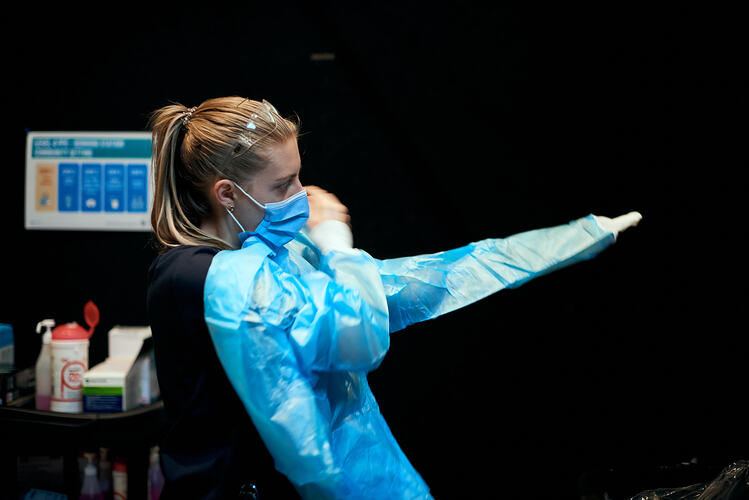 Staff member putting on Gown, St Vincent's Vaccination Hub, Melbourne Museum, 23 Sep 2021