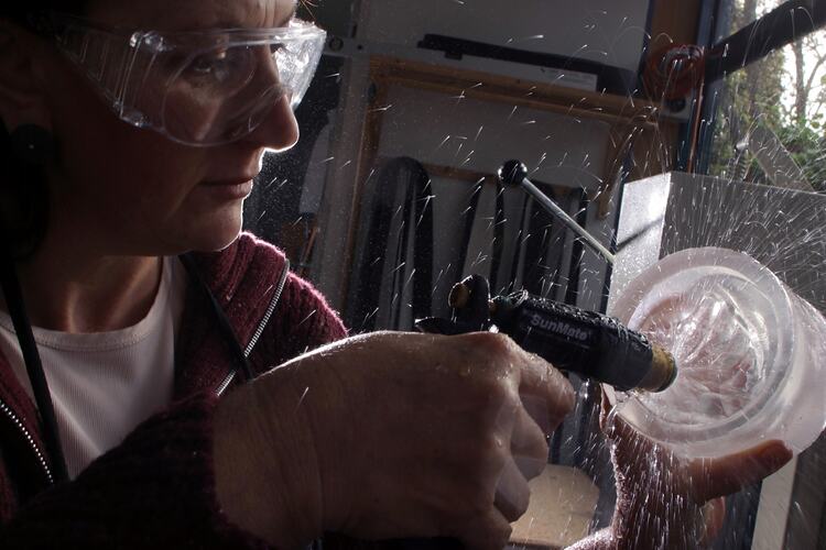 Woman wearing goggles spraying water into a glass bowl with a handheld spray gun.