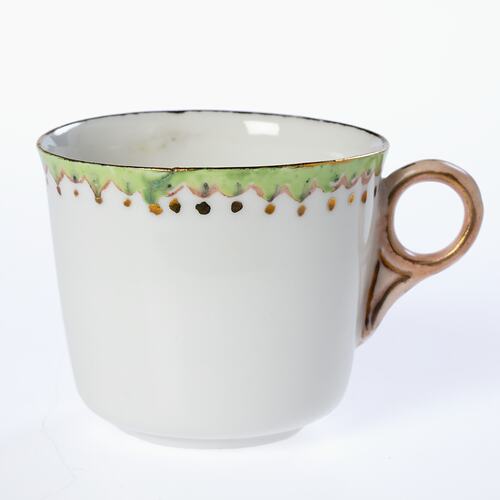 White tea cup with green, pink and gold decorated rim. Gold painted handle.