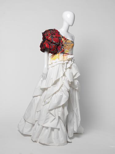 White ruffled wedding dress with oversized red butterfly-like right shoulder detail. Three quarter view.