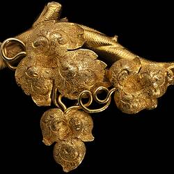 Ornate gold brooch with vine leaves on a branch.
