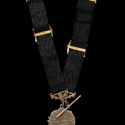 Back of gold fob with two black ribbed straps, each with a central gold shield-shaped slide and gold clips at top ends. The decorative heart-shaped fob is engraved with a running footballer holding a football.
