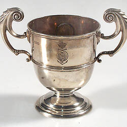 Silver cup with reeded girdles, harp-shaped handles. Royal Navy crest and medal inset.