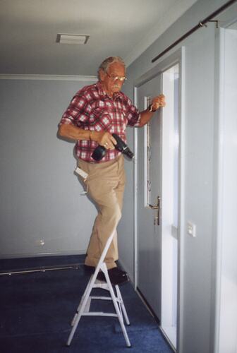 Man standing on ladder holding an electric drill.
