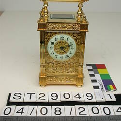 Ornate gold clock with handle on top.