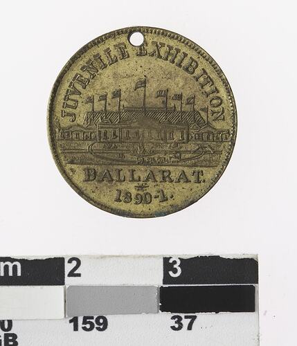 Round gold coloured medal with building and text.