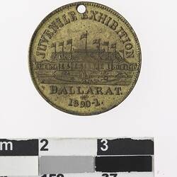 Round gold coloured medal with building and text.