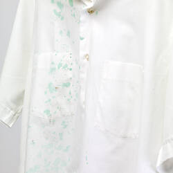 White button up short sleeve shirt with green paint splatter marks.