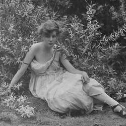 Black and white photograph of a girl in white dress next to a wattle tree.