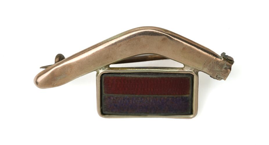 Brooch with bent gold boomerang above red and purple rectangle.