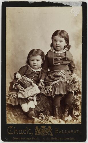 Two seated girls wearing dresses.