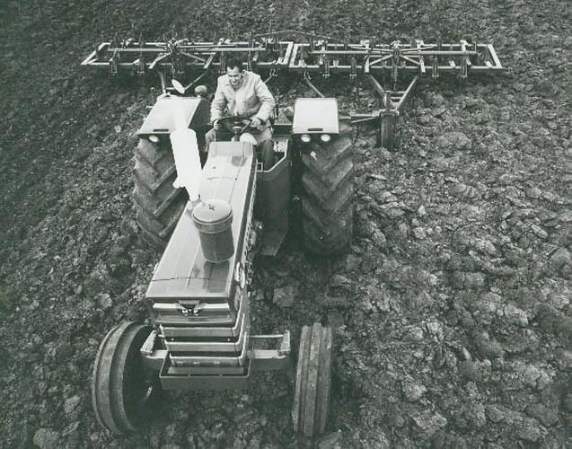 A man driving a  tractor coupled to a plough over rough ground.
