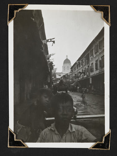 Two children in foreground, street and buildings in background.