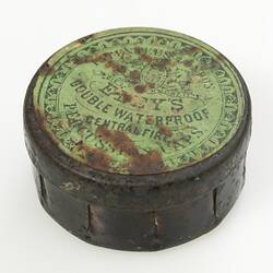 Round tin with worn yellow text on lid. Eley percussion cap tin.