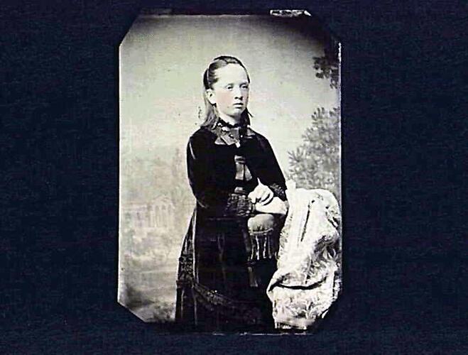 Standing girl, leaning on chair.