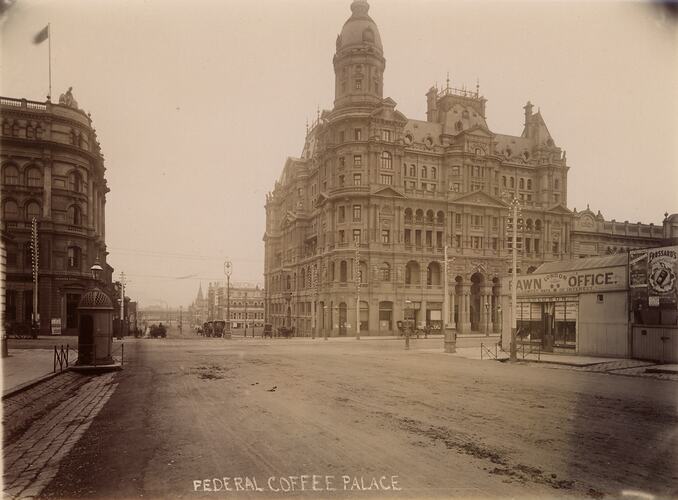 City street corner with ornate buildings. A small metal structure, possibly a public toilet is located on the leftside street corner.