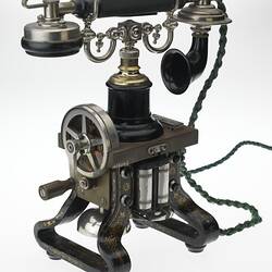 Iron telephone painted black with gold details. Dial at side. Green plaited cords.