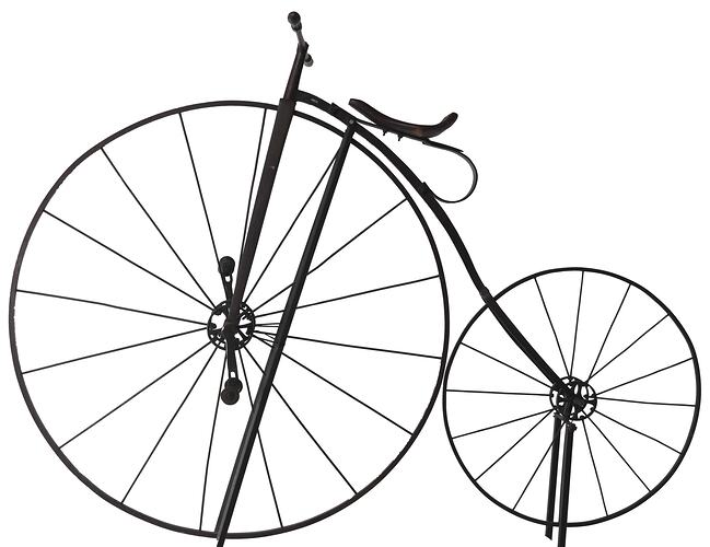 Iron bicycle painted black with large front wheel and small rear wheel. Seat on large front wheel.