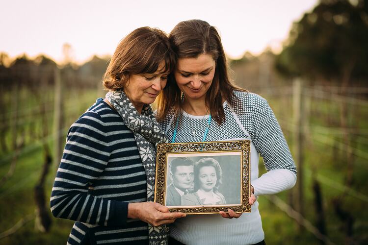 Two women in vineyard holding framed photograph.