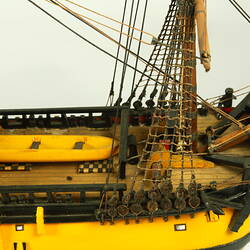 Detail of front of deck on model ship with wooden hull painted yellow.
