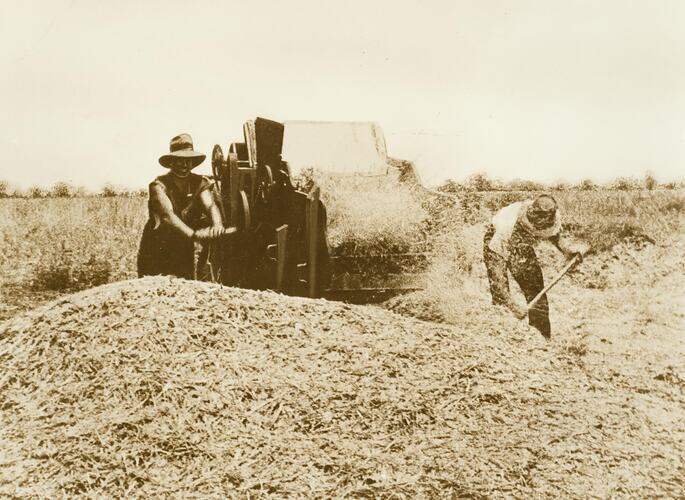 Two men hand operating a winnower.