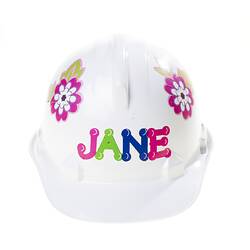 White plastic hard hat with multi-colour flower stickers on side and letter stickers on front. Front view.