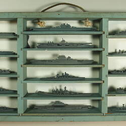 One half of a wooden bifold case painted blue-grey with rope handle. Contains 16 grey ship models in 3 columns