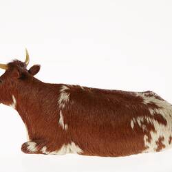 Model of seated brown and white cow. Left profile.