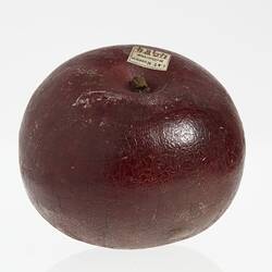 Wax apple model painted dark red. Has short stem and paper label affixed on top.