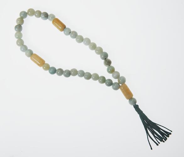 Beaded loop with pale blue, grey, yellow and white beads. Black tassel at end.