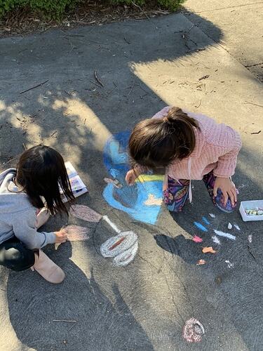 Two girls drawing with coloured chalk on the driveway.