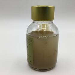 Glass bottle with gold lid. Contains thick, cloudy brown liquid.