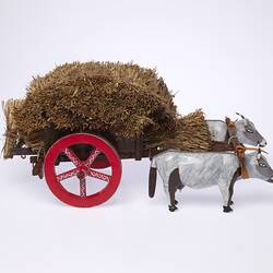 Model of two grey bullocks pulling a hay wagon with haystack and red wheels. Right profile view.