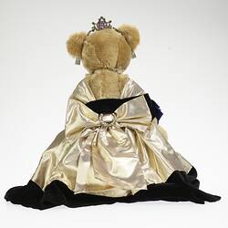 Back of light brown bear in black velvet and gold lame gown. Faux diamond, amethyst tiara, necklace, earrings.