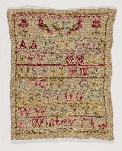 Embroidered sampler of coloured alphabet on a woven cream fabric ground. Birds and flowers at top.