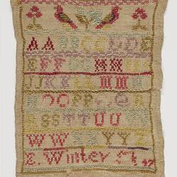 Embroidered sampler of coloured alphabet on a woven cream fabric ground. Birds and flowers at top.