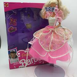 Barbie doll with layered pink dress. Purple and pink box behind her.