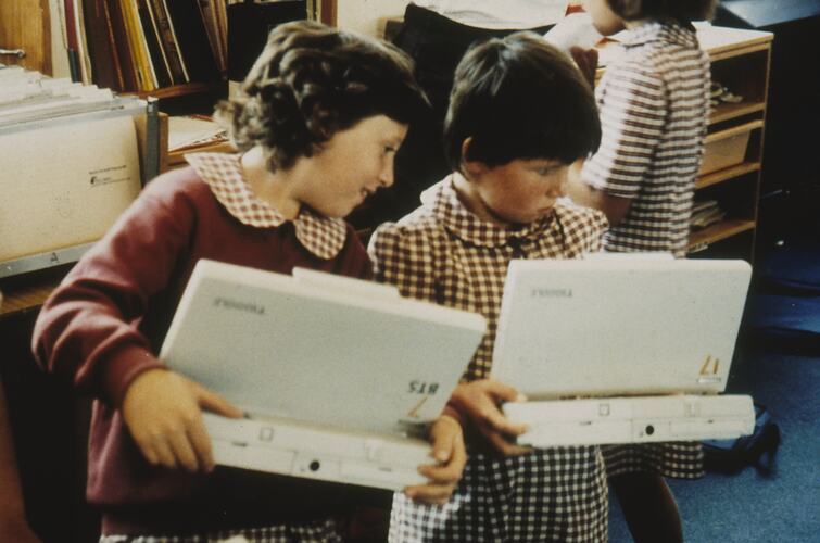 Two young girls in school uniform with laptops.