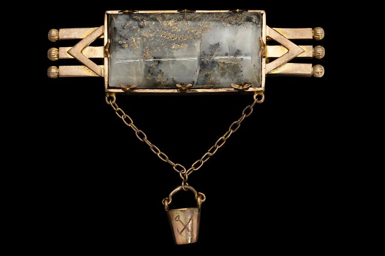 Triple bar brooch with central quartz and gold specimen with small gold bucket attached via chain.