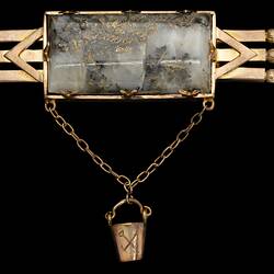 Triple bar brooch with central quartz and gold specimen with small gold bucket attached via chain.