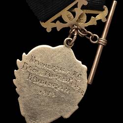 Detail of back of gold heart-shaped fob with engraved text. Gold attachments and short chain.