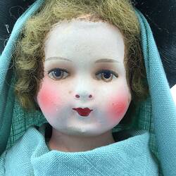 A doll dressed in a long green gown, veil and hat