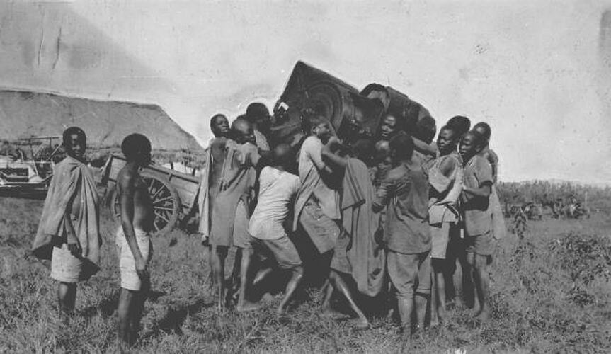 "ASSEMBLING A HEADER ON LORD HOWARD DE WALDEN'S ESTATE, KENYA COLONY: 30 NATIVES CARRYING THE DRUM AND DRUMCASE"