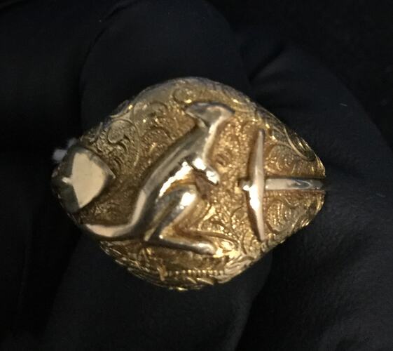 Gold ring with a kangaroo facing right. Miner's shovel on it's left and pick on it's right.