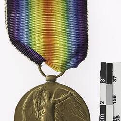 Round medal with winged woman and rainbow ribbon attached.