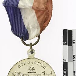 Round medal with Australian coat of arms and text, with red, white and blue ribbon attached.