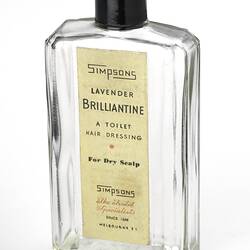 Small clear glass rectangular bottle with black lid. Printed paper label, red text. Yellow liquid in bottle.