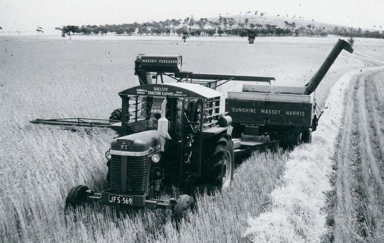Front view of a  tractor coupled to a harvester, unloading to a grain field bin.