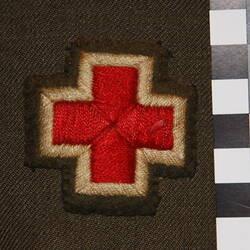 Patch with red cross and white border stitched onto green felt on Khaki wool fabric