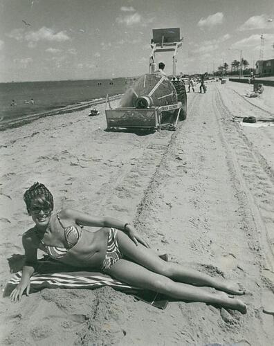 Woman lying on beach in front of beach cleaner.